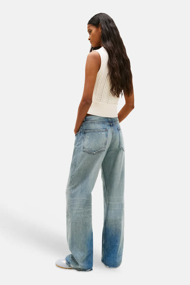 Débardeur blanc de TOMMY JEANS, en tricot torsadé, porté avec un jean bleu délavé à jambes larges.