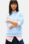 Sweat-shirt bleu par TOMMY JEANS avec superposition d'une chemise rayée rose et blanche.