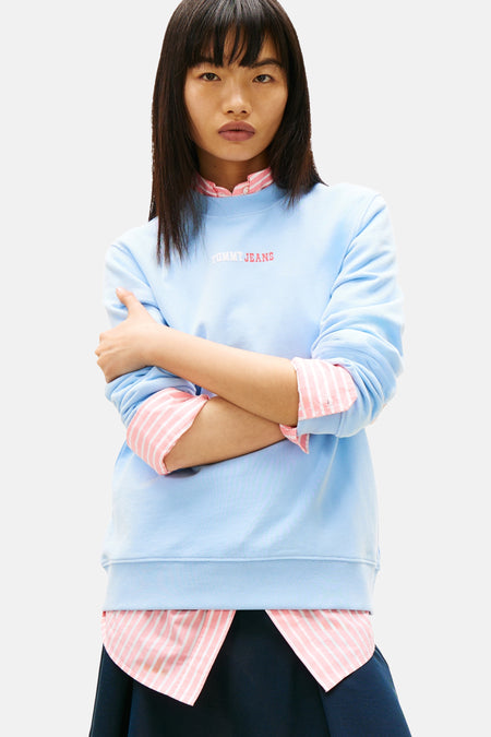 Sweat-shirt bleu par TOMMY JEANS avec superposition d'une chemise rayée rose et blanche.
