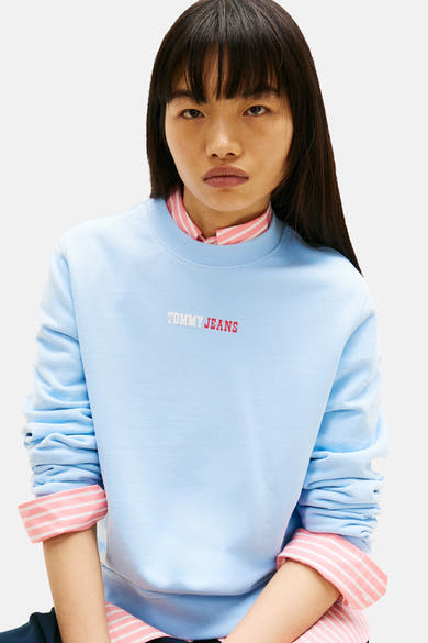 Sweat-shirt bleu de TOMMY JEANS, avec un col rond et inscription rouge « TOMMY JEANS » sur le devant, porté par une femme.