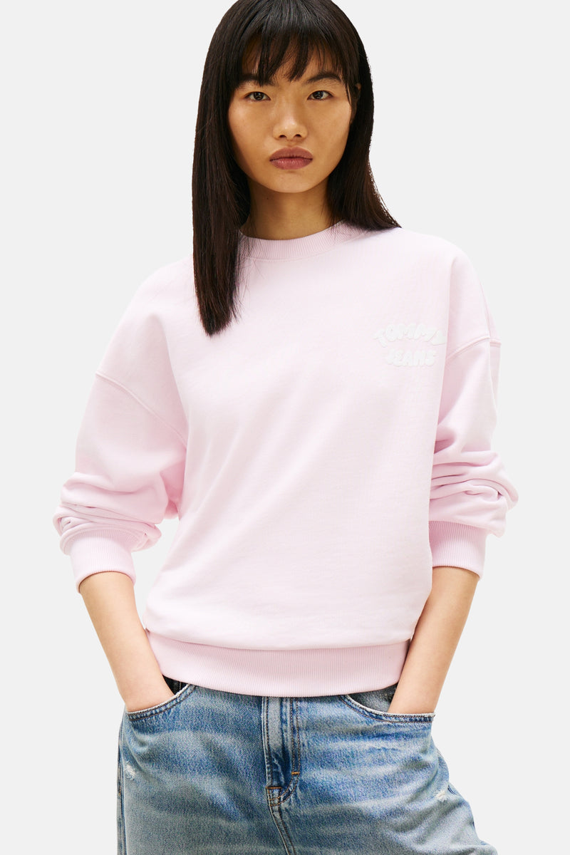 Sweatshirt van TOMMY JEANS, gedragen met een wijde spijkerbroek en roze sneakers.