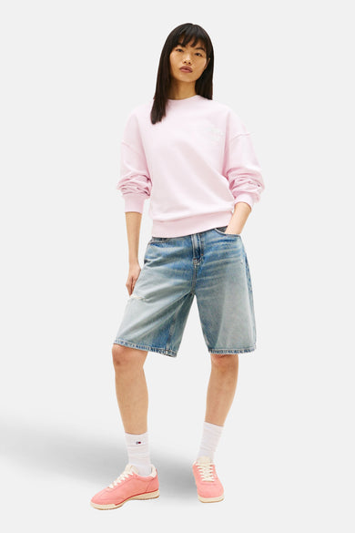 Sweat rose de TOMMY JEANS, porté avec un short en jean ample et des baskets roses.