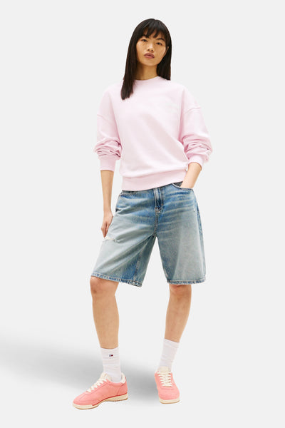 Sweat rose de TOMMY JEANS, porté avec un short en jean ample et des baskets roses.