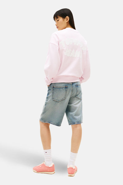 Sweatshirt van TOMMY JEANS met een wit logo op de rug, gedragen met een spijkerbroekshort.