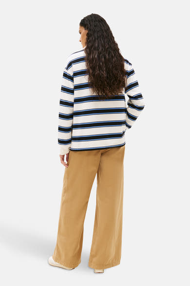 Multikleurig poloshirt met lange mouwen van TOMMY JEANS, zwarte en blauwe horizontale strepen op een witte achtergrond, gedragen met een beige broek.