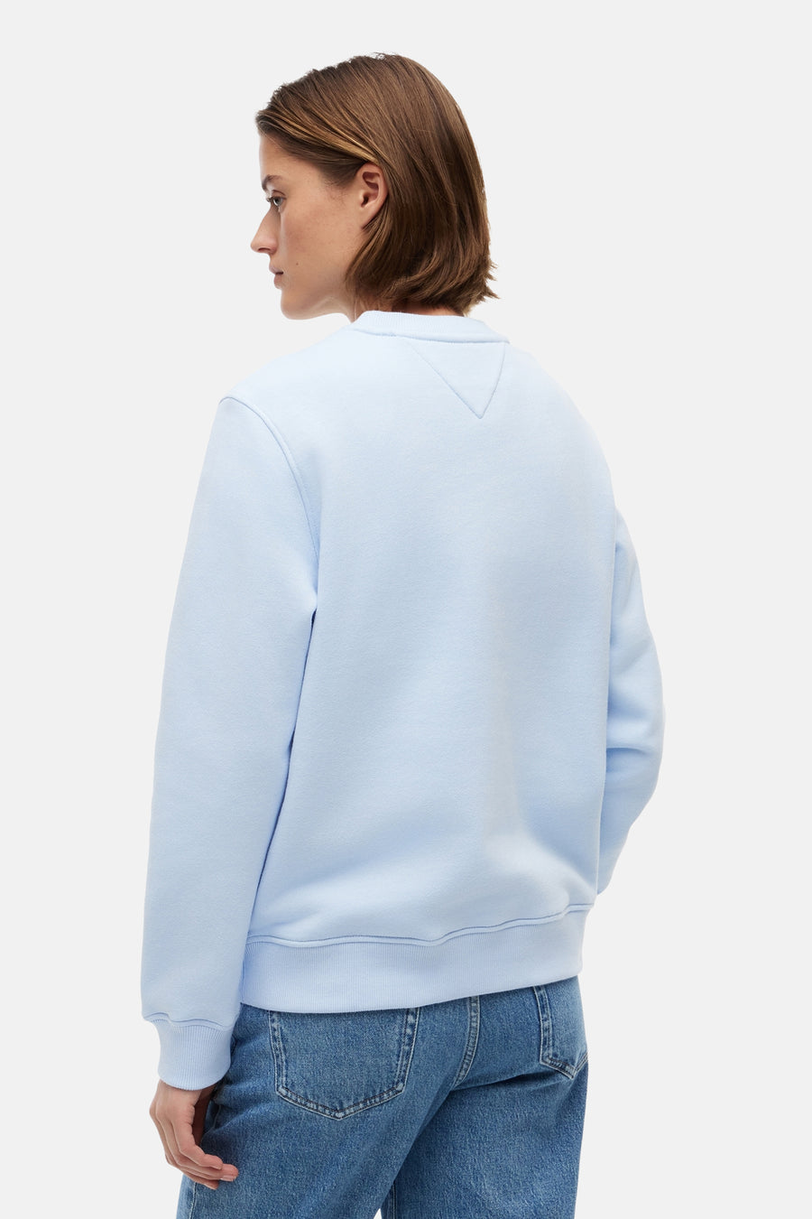 Lichtblauwe sweater van TOMMY JEANS, achterkant met V-inzet onder de kraag, gedragen met een blauwe jeans.