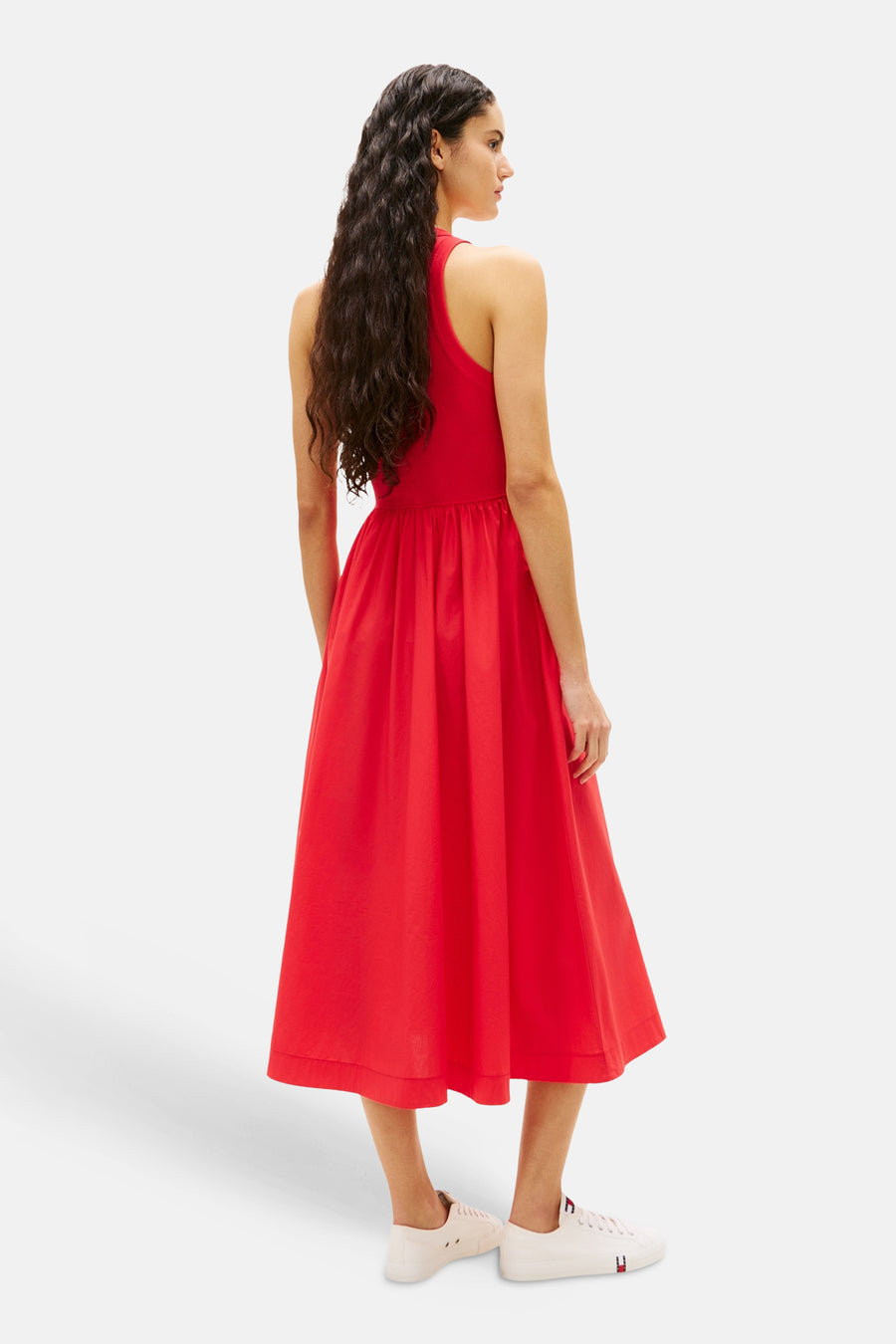 Robe rouge de TOMMY JEANS, avec une coupe évasée et longueur midi, portée avec des chaussures blanches.

