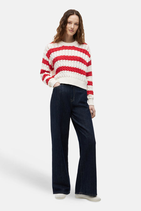 Ronde hals trui van TOMMY JEANS in wit en rood, met horizontale textuurstrepen, gedragen met een donkere jeans.