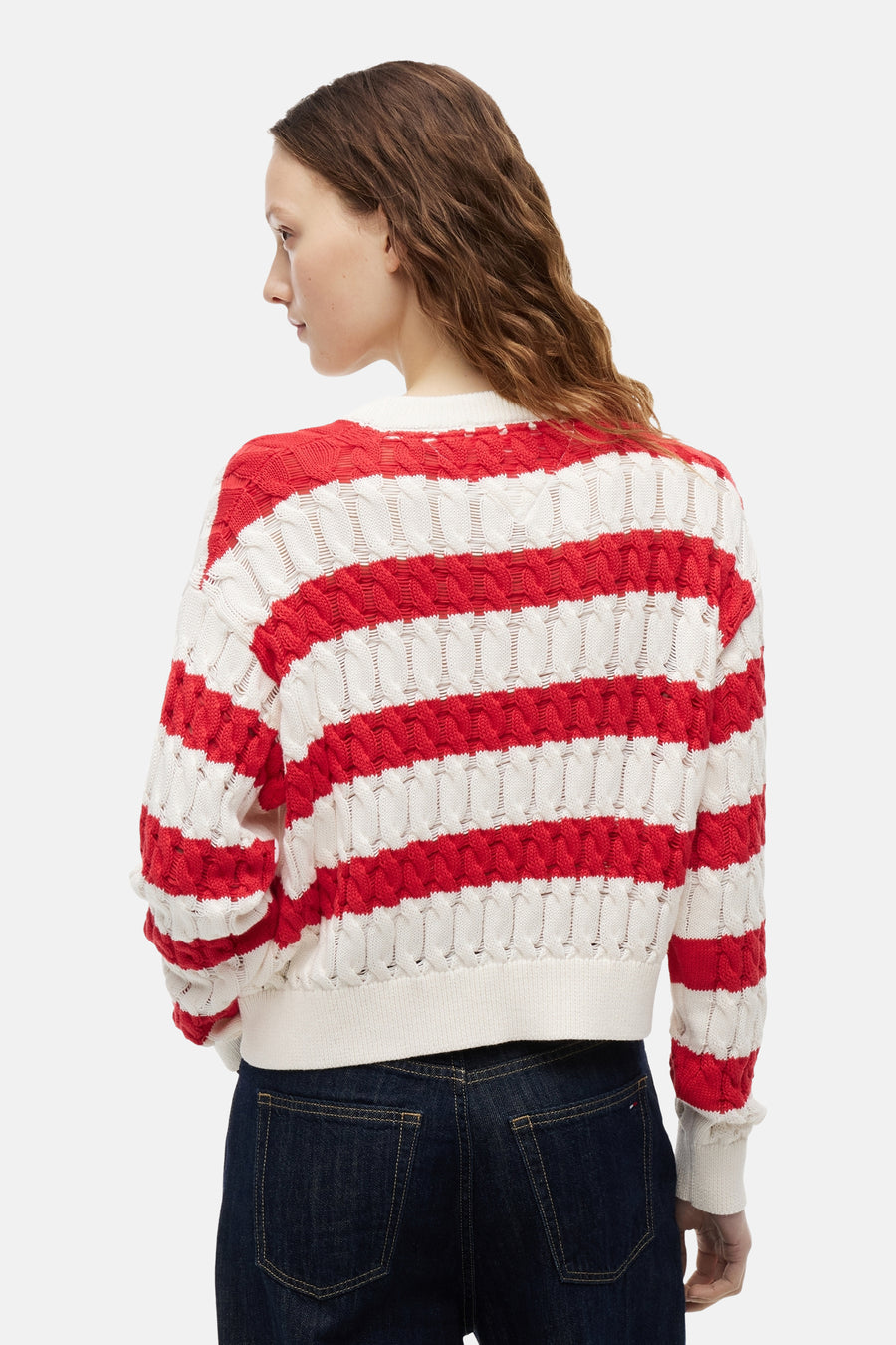 Wit-rood gestreepte trui met ronde hals van TOMMY JEANS in opengebreide stof, van achteren gezien, gedragen met een donkere spijkerbroek.