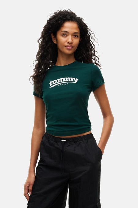 Dark green short-sleeve cropped T-shirt by Tommy Jeans with white logo, worn with black drawstring pants, front view.