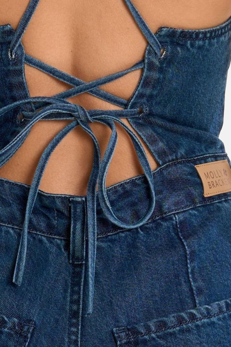 Combinaison en jean bleu moyen de Molly Bracken avec laçage et nœud à nouer dans le dos, patch de marque visible.