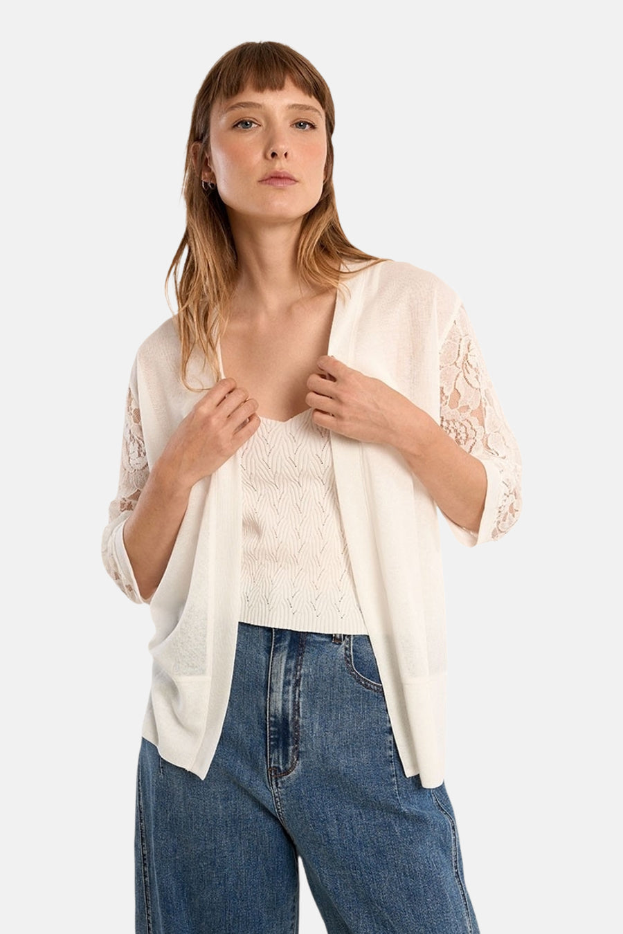 Cardigan blanc par Molly Bracken avec manches en dentelle porté sur un débardeur et un jean.