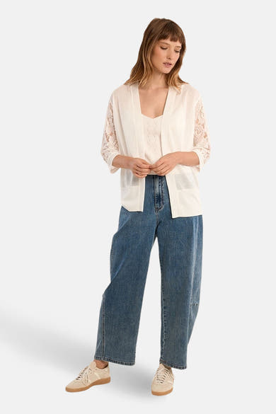 Cardigan blanc de Molly Bracken, avec manches en dentelle florale, porté sur un débardeur et un jean large.