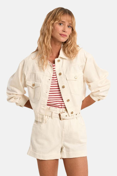 Veste en jean blanche de Molly Bracken, courte, à boutons dorés, portée sur un haut rayé avec un short assorti.