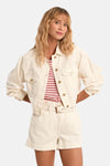 Veste en jean blanche de Molly Bracken, courte, à boutons dorés, portée sur un haut rayé avec un short assorti.