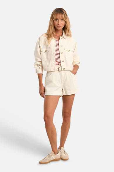 Veste en jean blanche de Molly Bracken, courte avec boutons dorés, portée avec un t-shirt rayé et un short assorti.