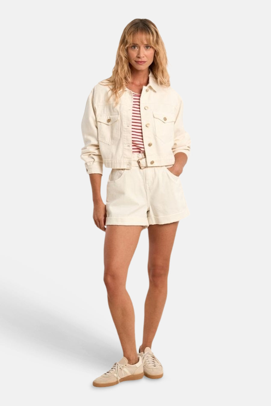Veste en jean blanche de Molly Bracken, courte avec boutons dorés, portée avec un t-shirt rayé et un short assorti.