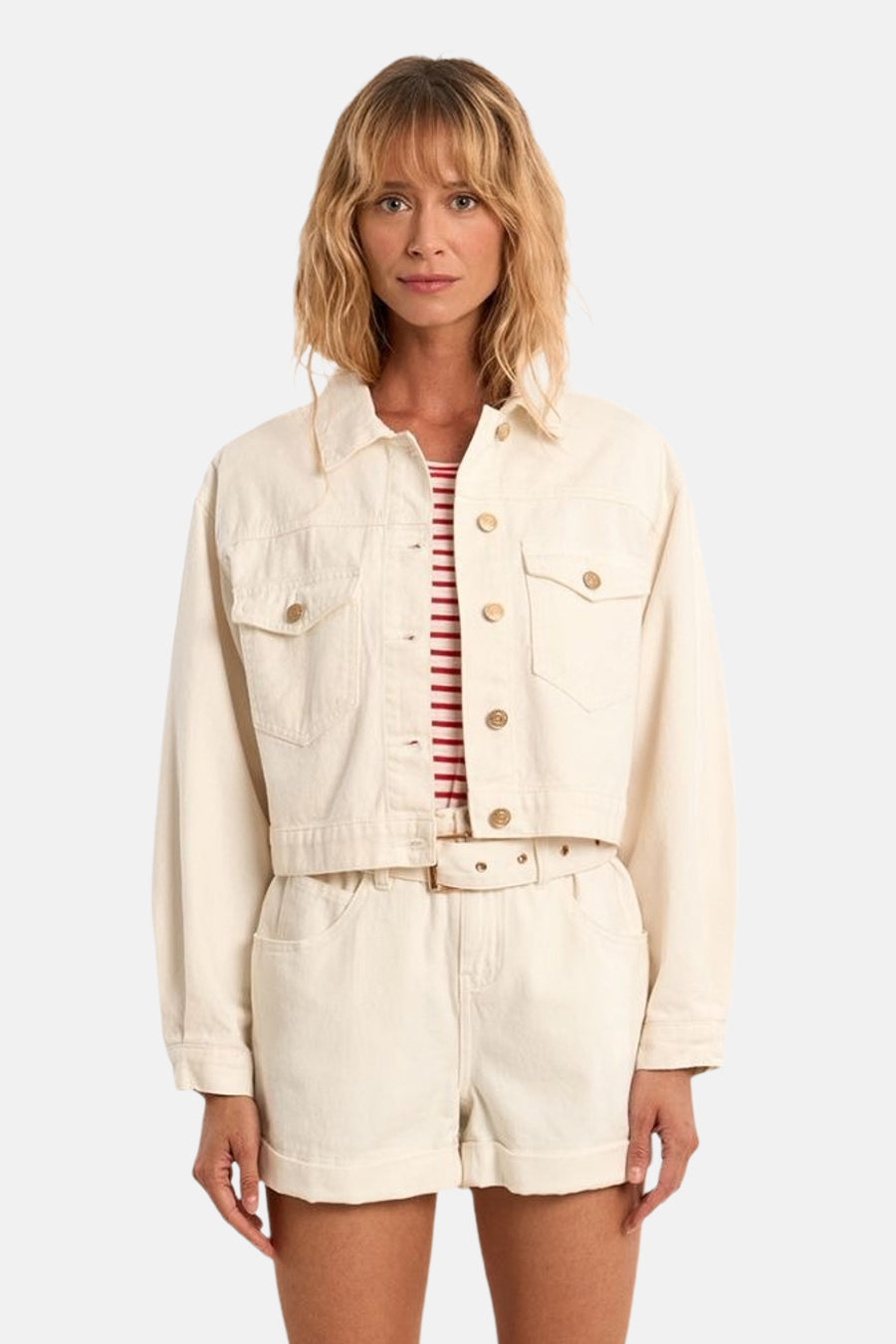 Veste en jean blanche de Molly Bracken, coupe courte avec boutons dorés et poches poitrine, portée sur un top rayé et un short assorti.