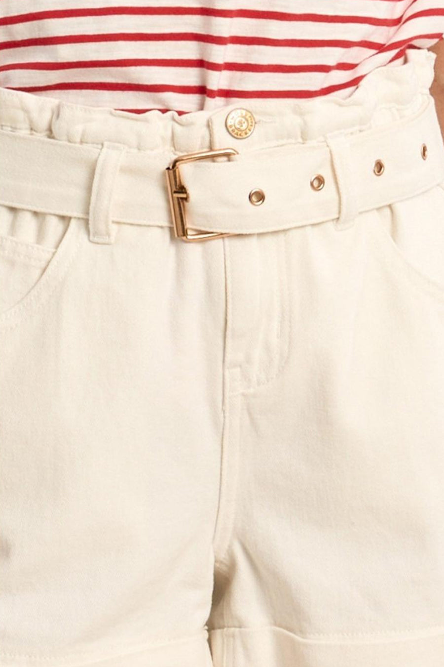 Short blanc de Molly Bracken à taille haute froncée, ceinture à boucle dorée et poches. Porté avec un haut rayé rouge et blanc.