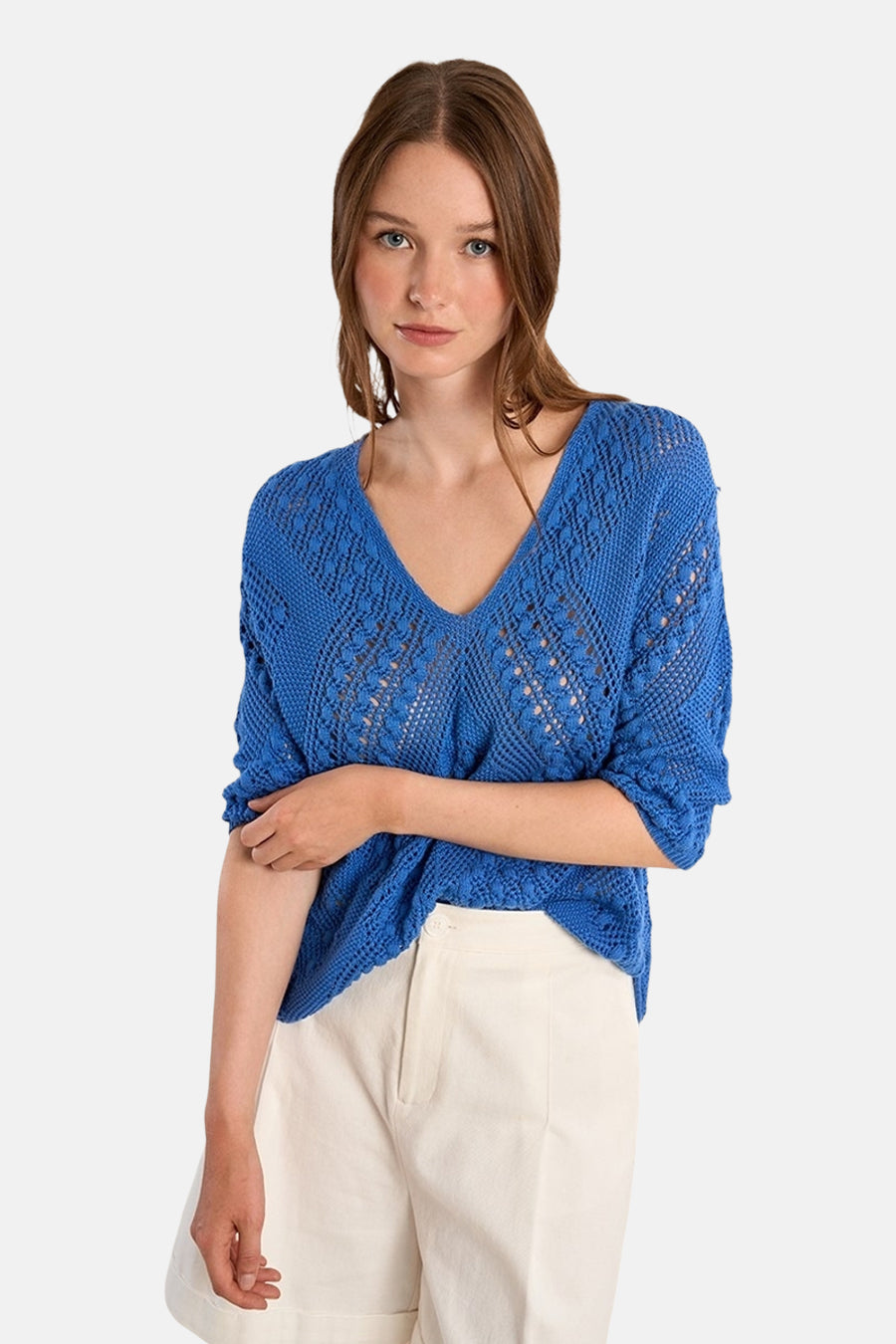 Blauwe V-hals trui, van Molly Bracken, met een open gebreid patroon en gedragen met een witte short.