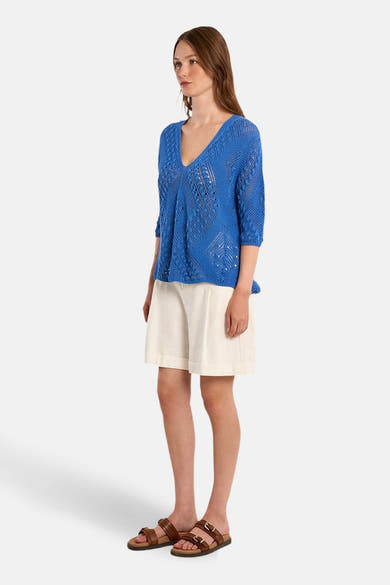Molly Bracken blauwe V-hals trui met een opengebreid patroon, gedragen met een beige short en bruine sandalen.