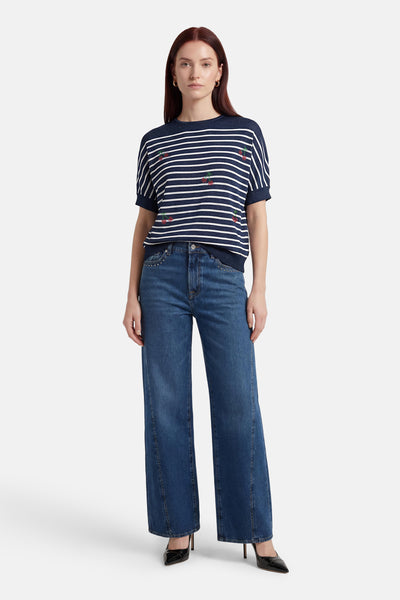 Pull multicolore col rond de Molly Bracken, orné de motifs cerises et porté avec un jean évasé bleu et des escarpins noirs.