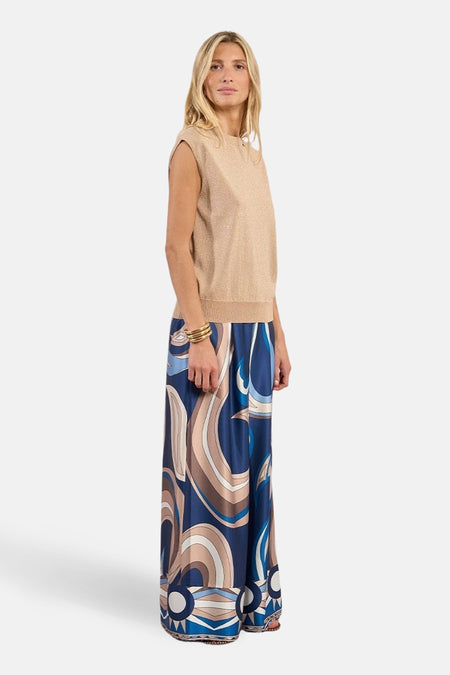 Top sans manches beige de Molly Bracken avec une texture scintillante, porté avec un pantalon à motif tourbillonnant.