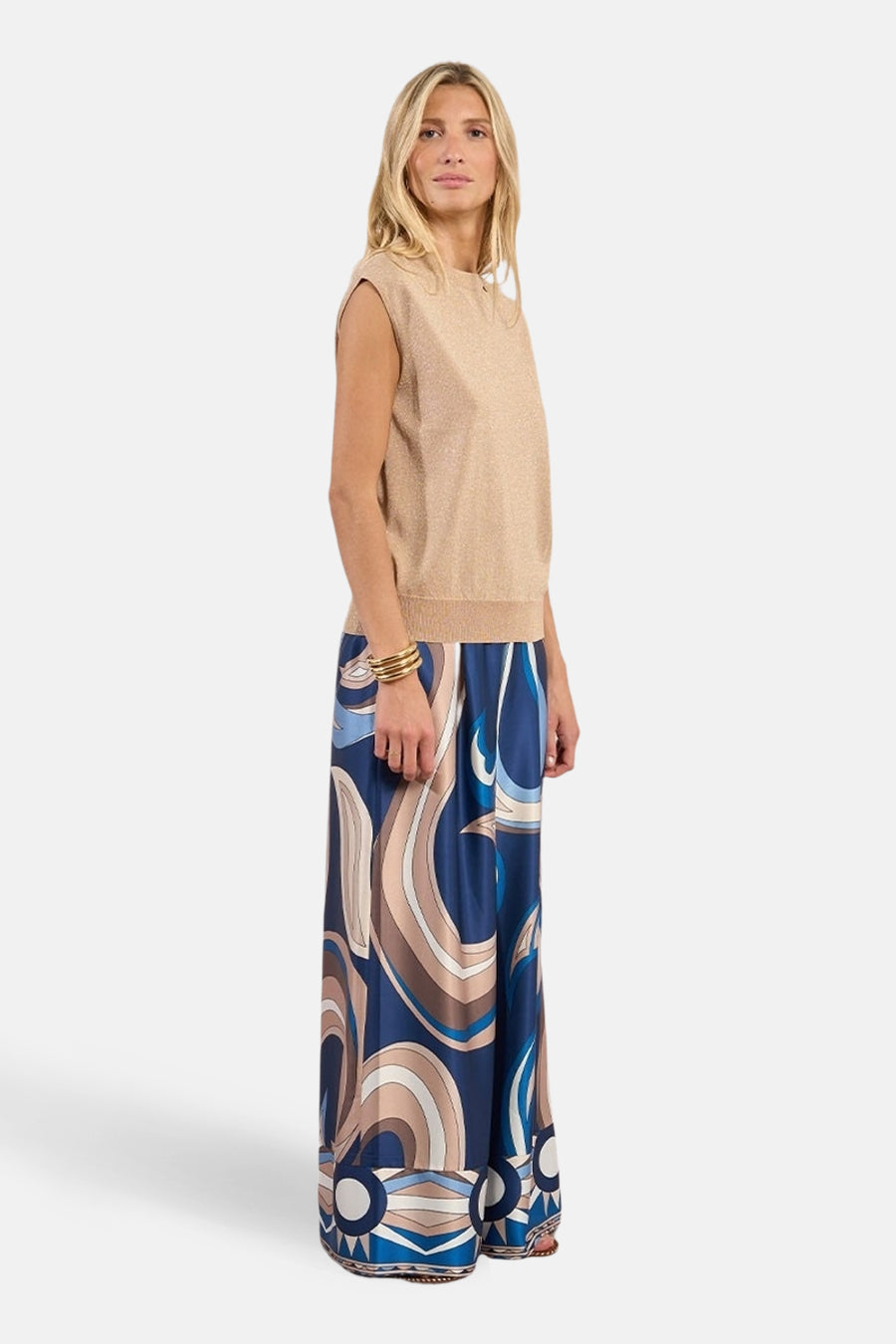 Top sans manches beige de Molly Bracken avec une texture scintillante, porté avec un pantalon à motif tourbillonnant.