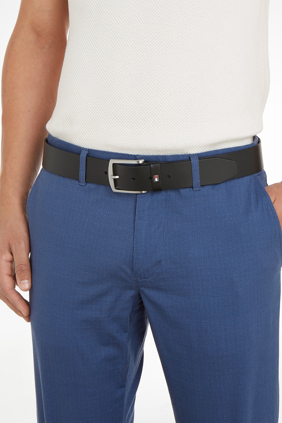 Ceinture noire par TOMMY JEANS avec boucle argentée, portée avec un pantalon texturé bleu et une chemise blanche.
