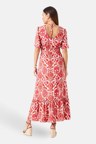 Lange veelkleurige jurk van GARCIA, rood en roze paisley-motief, lage rug, gedragen met sleehakken.