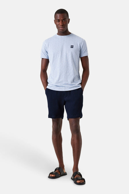 Blauwe T-shirt met korte mouwen van GARCIA, met geometrisch patroon op een man die een marineblauwe korte broek en sandalen draagt.