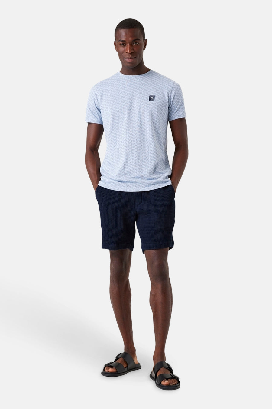 Blauwe T-shirt met korte mouwen van GARCIA, met geometrisch patroon op een man die een marineblauwe korte broek en sandalen draagt.