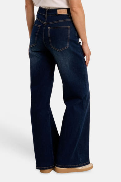 Jean large en denim bleu moyen de Molly Bracken, vue arrière, taille haute, avec surpiqûres contrastantes, étiquette en cuir et baskets beiges.