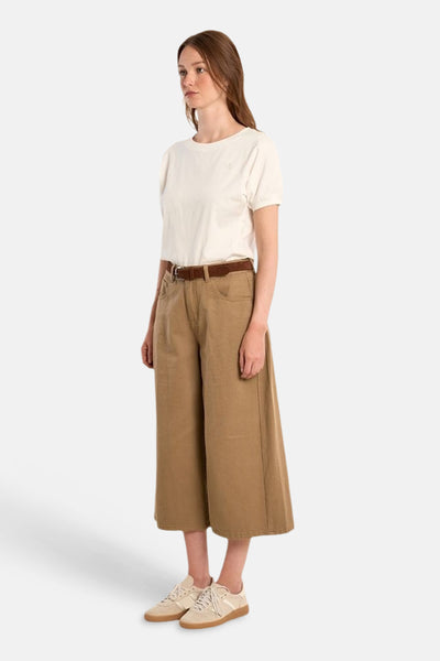 Wijde kaki broek van Molly Bracken, gesneden, gedragen aan de zijkant met een crèmekleurig T-shirt, een bruine riem en crèmekleurige sneakers.
