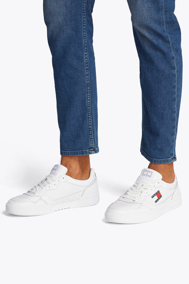 Witte TOMMY JEANS sneakers, gedragen met een blauwe jeans, kleurrijk logo aan de zijkant.
