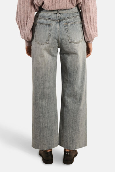 Wijde spijkerbroek in middieblauw denim van Molly Bracken, met achterzakken en een rafelzoom, gedragen met een roze trui.