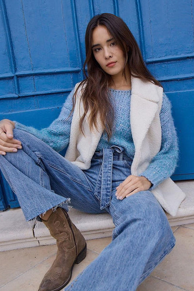 Jean large en denim bleu moyen de Molly Bracken, porté avec un pull bleu et un gilet blanc.