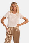 Top uni manches courtes blanc de Molly Bracken, porté avec un pantalon doré satiné.