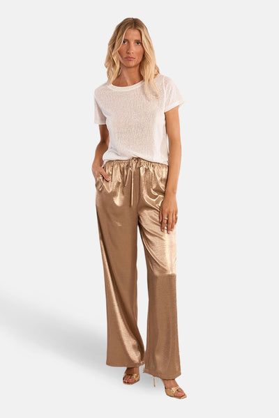 Top uni manches courtes blanc de Molly Bracken porté avec un pantalon doré fluide et des sandales à talons.