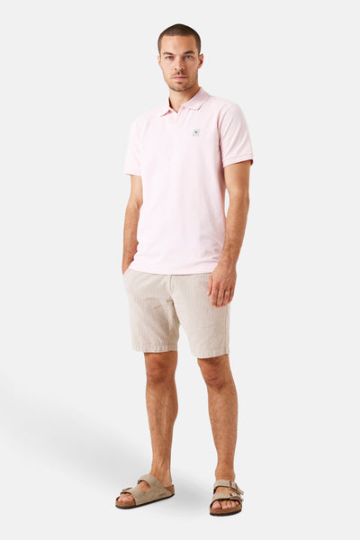 Polo à manches courtes rose de GARCIA, porté avec un short beige rayé et des sandales en daim.