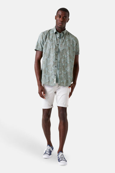 Chemise kaki à manches courtes de GARCIA, avec un motif de feuilles, portée avec un t-shirt uni et un short blanc.