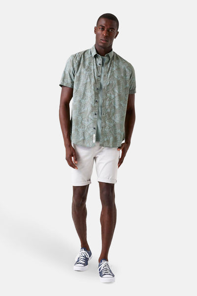 Chemise kaki à manches courtes de GARCIA, avec un motif de feuilles, portée avec un t-shirt uni et un short blanc.