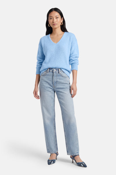 Pull à col en V bleu d'AMELIE ET AMELIE porté avec un jean et des chaussures à talons bleues.