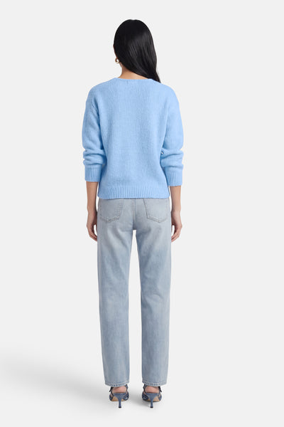 Pull à col en V bleu d'AMELIE ET AMELIE, vue arrière, porté avec un jean clair et des chaussures à talons bleues.