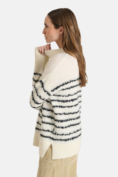 Pull rayé en maille douce de Le Temps des Cerises, avec col montant et manches longues, porté avec un pantalon beige.