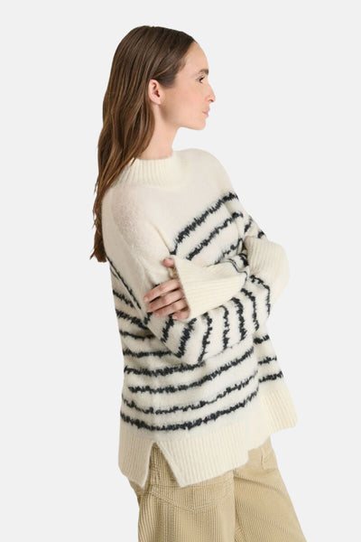 Pull en laine rayé blanc cassé et noir de Le Temps des Cerises, porté avec un pantalon beige en velours côtelé.