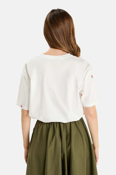 T-shirt blanc à manches courtes de Le Temps des Cerises, orné de cerises brodées aux manches, porté avec une jupe olive.