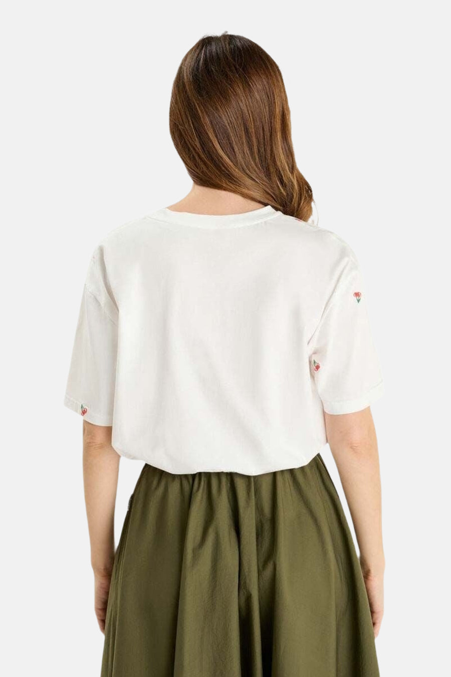 T-shirt blanc à manches courtes de Le Temps des Cerises, orné de cerises brodées aux manches, porté avec une jupe olive.