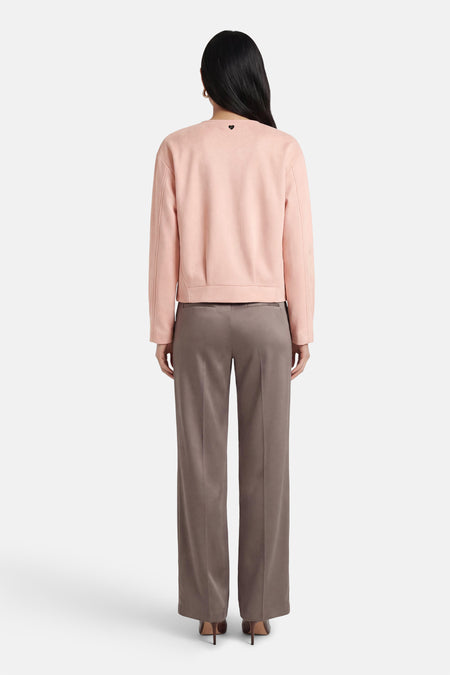 Veste courte rose d'AMELIE ET AMELIE avec un petit cœur noir sur le dos, portée avec un pantalon marron.
