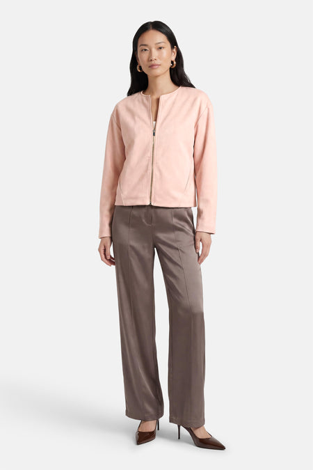 Veste courte rose van AMELIE ET AMELIE, avec fermeture éclair et style élégant, portée avec un pantalon marron et des escarpins vernis.
